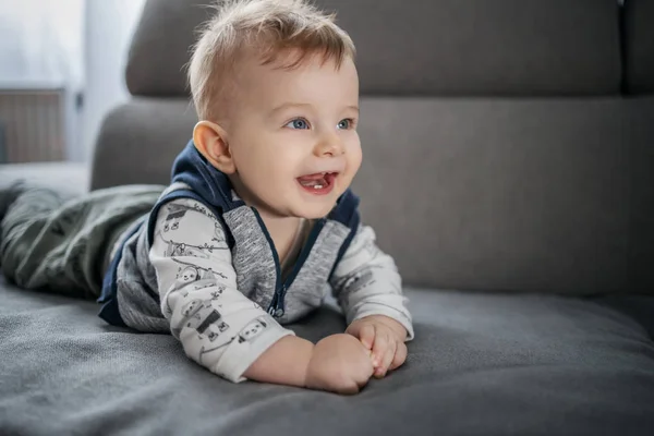 陽気な幸せな小さな赤ちゃん男の子笑顔と嘘上の胃の上にソファでリビングルーム — ストック写真