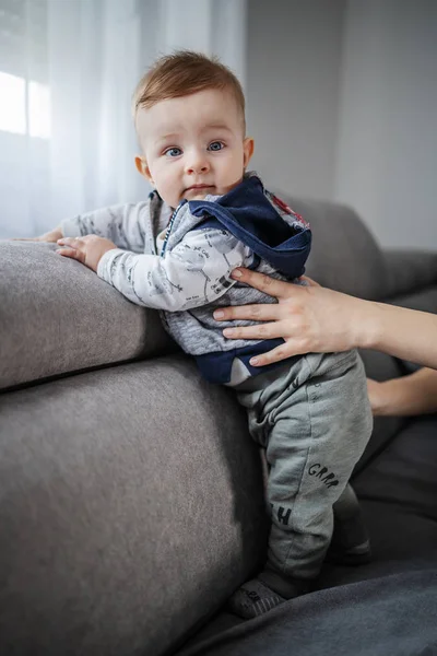 可爱的幼儿在妈妈的帮助下站在沙发上 — 图库照片