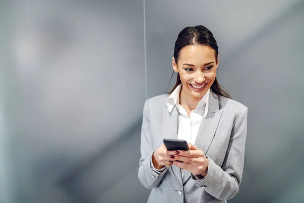 年轻迷人的 面带微笑的高加索女商人站在公司内部 用智能手机向她的商业伙伴传递信息 — 图库照片