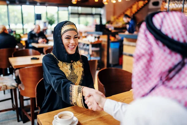 男性ビジネスパートナーと握手をする伝統的なウェアを身に着けているかわいい笑顔の肯定的なアラブ女性 コーヒーショップのインテリア 多様性の概念 — ストック写真