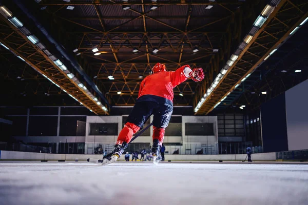 Rear view of hockey player skating towards opposite team and trying to score. Hall interior.