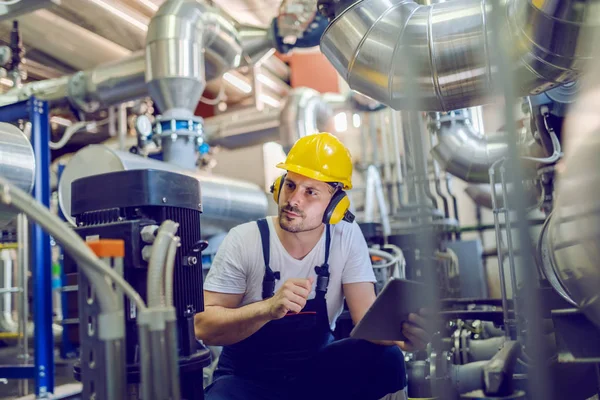 Serious Caucasian Handsome Worker Overall Hardhat Antiphons Crouching Holding Tablet — 스톡 사진