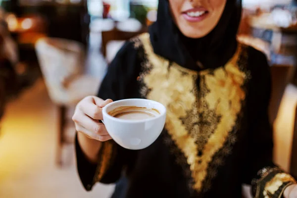 伝統的な服を着た笑顔のアラブ女性がカフェに座って新鮮なエスプレッソを飲んで閉じます 週末の無料時間 — ストック写真