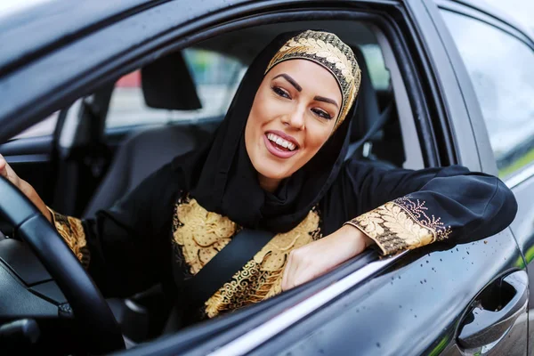 迷人的病人微笑着年轻的穆斯林女子坐在她的车里 在交通堵塞中等待 — 图库照片