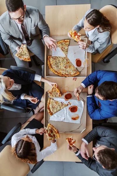 テーブルに座って昼食にピザを食べておしゃべりするビジネスマンのグループのトップビュー — ストック写真