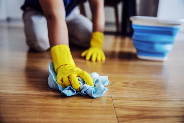 Close up of man waxing parquet. Selective focus on hand with cloth. Rubber gloves on hands. Home interior.