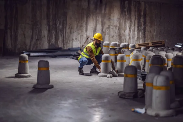 施工过程中蹲伏在隧道中 头戴钢盔 头戴混凝土柱的年轻带胡子工人 — 图库照片
