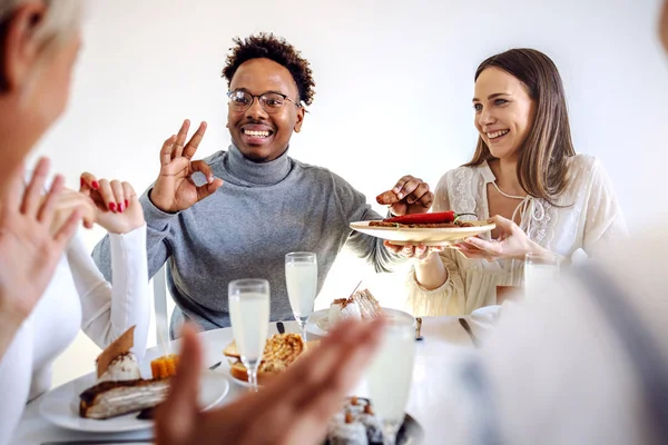 魅力的な笑顔アフリカ系アメリカ人の男性は 食事のテーブルに座って プレートから肉のロールを取り 大丈夫な兆候を示しています ブルネット保持板 — ストック写真