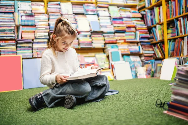 Urocza Biała Dziewczynka Siedząca Podłodze Księgarni Czytająca Opowiadania Półkach Książki — Zdjęcie stockowe