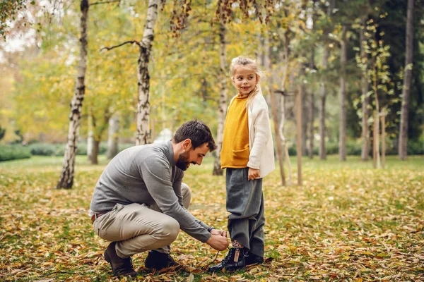 慈爱的父亲蹲着 把鞋带绑在女儿的鞋子上 女孩的目光移开 秋天的公园时间 — 图库照片