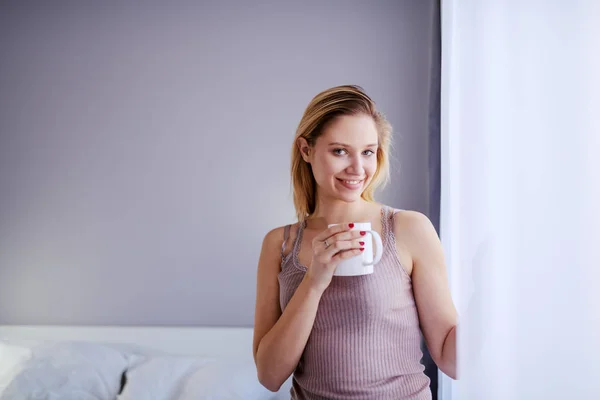 Young Caucasian Smiling Blond Woman Standing Next Window Holding Mug — Stock Photo, Image