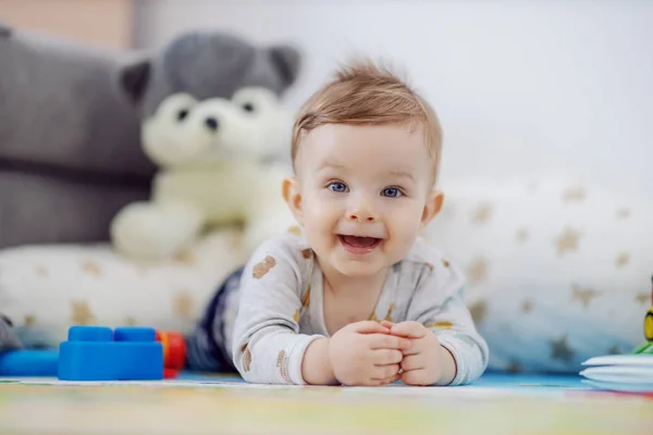 愛らしい笑顔遊び心のある男の子とともに青い目が胃の上に横たわってカメラを見て — ストック写真