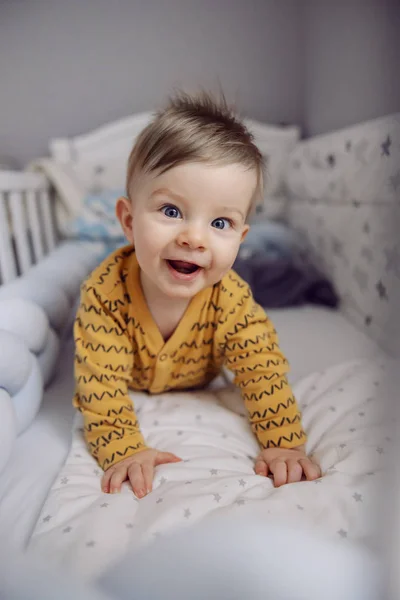 美しいです明るいですブロンド幼児とともに青い目嘘上の胃の上に彼のクリブで午前中 — ストック写真