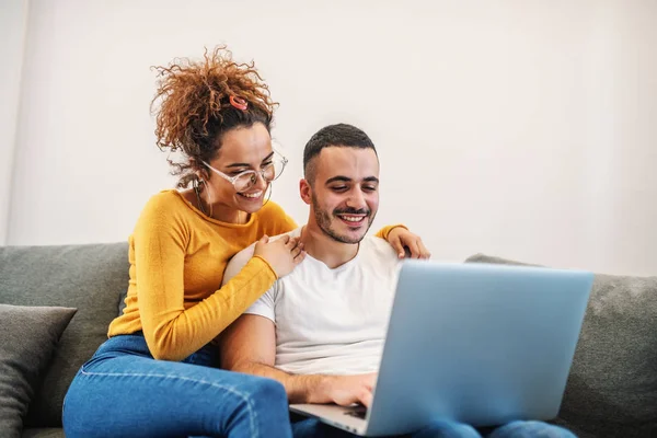 Young attractive happy couple sitting at home and surfing on internet over laptop.