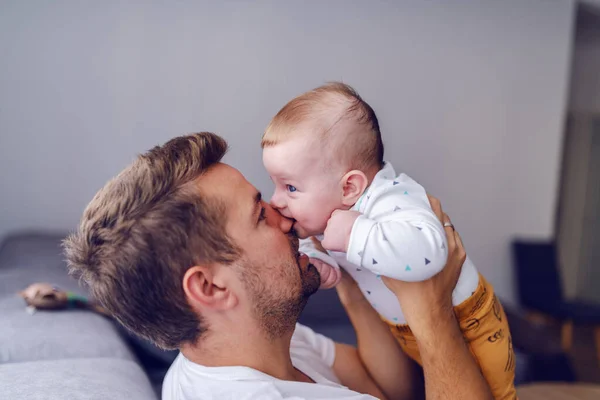 接近可爱的6个月大的高加索男婴咬爸爸的鼻子 英俊的年轻爸爸抱着孩子 牙齿成长的概念 — 图库照片