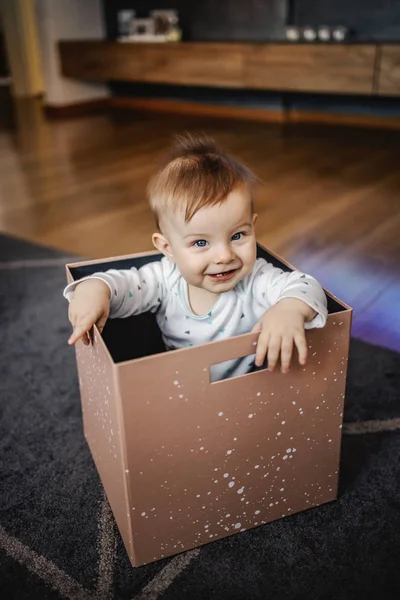 可爱的金发小男孩 蓝眼睛坐在盒子里 玩耍着 看着镜头 家庭内部 — 图库照片