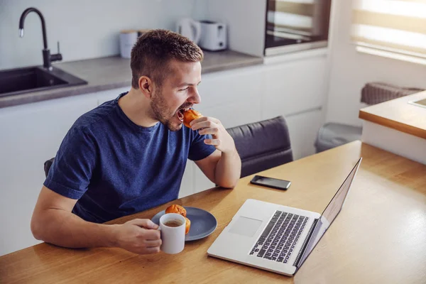 Junger Schöner Bärtiger Mann Sitzt Esstisch Frühstückt Und Schaut Nachrichten — Stockfoto