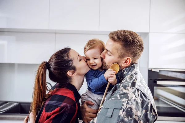 Young soldier arrived home and he is happy with his family. Man and woman kissing their beloved only son.