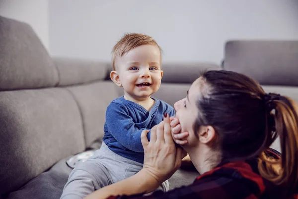 幸せな息子はソファに座って母親と遊ぶのが大好きでした 彼は彼女の顔に触れ 大きなおもちゃの笑顔でカメラを見ている — ストック写真