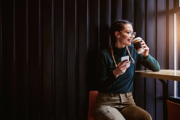 Lächelnde Frau Sitzt Cafeteria Neben Fenster Trinkt Kaffee Und Hält — Stockfoto