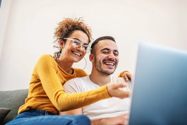 若い魅力的な幸せなカップルは自宅に座って ラップトップ上でインターネットでサーフィン 女性あります抱擁彼女の最愛のボーイフレンド — ストック写真