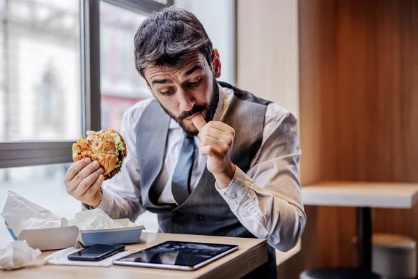 Éhes Ember Öltönyben Gyorskajáldában Ebédszünetben Sajtburgert Eszik Híreket Olvas Tableten — Stock Fotó