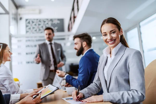 Ung Smilende Hardtarbeidende Forretningskvinne Som Sitter Styrerommet Tar Notater Bakgrunnen – stockfoto