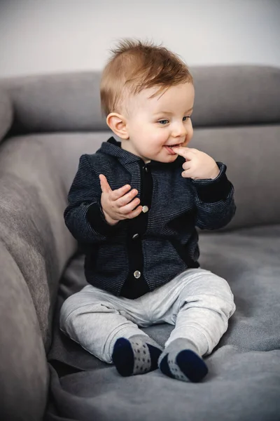 Cute Satisfied Little Blond Boy Sitting Sofa Putting Fingers Mouth — Zdjęcie stockowe