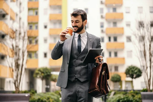 面带微笑的商人一边喝咖啡一边去工作 背景是建筑物 — 图库照片