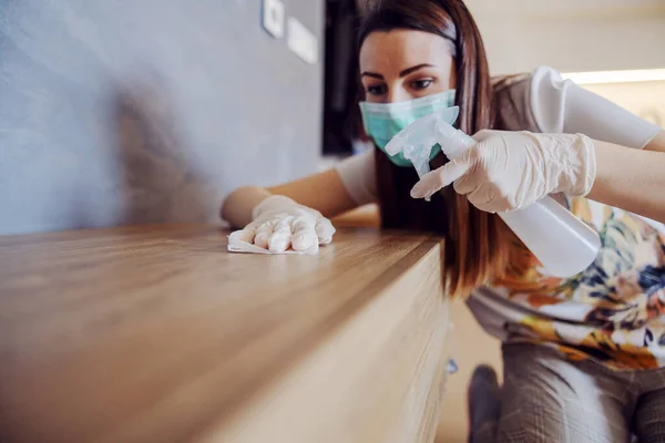 Woman cleaning shelf with antibacterial wipe and sanitizing agent for viruses on home surfaces. Corona virus preventive measures.