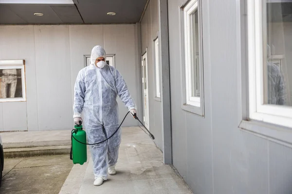 ウイルス保護服の男とマスクスプレーでコロナウイルスの建物を消毒する 感染予防と流行の制御 世界大流行 — ストック写真