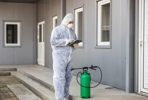 Mann Virenschutzanzug Und Maske Schaut Und Tippt Auf Tablette Desinfiziert — Stockfoto