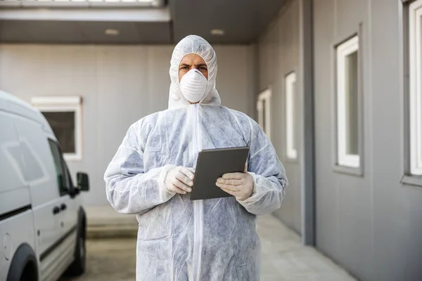 Mann Virenschutzanzug Und Maske Schaut Und Tippt Auf Tablette Desinfiziert — Stockfoto