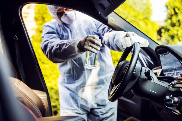 車内でマスク消毒と保護スーツの男 頻繁に触れられているきれいな表面を拭く Covid 19ウイルスコロナウイルスの感染を防ぐ 細菌や細菌の汚染 感染の予防と制御 — ストック写真