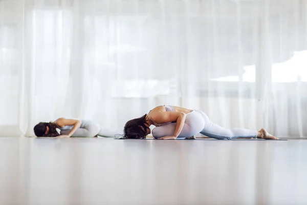 2人の魅力的なフィットヨギ女の子で寝て白鳥のヨガポーズ ヨガスタジオインテリア — ストック写真