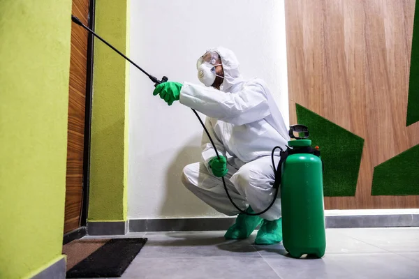 コロナウイルス コビットから建物のドアを滅菌保護スーツとマスクの労働者 — ストック写真