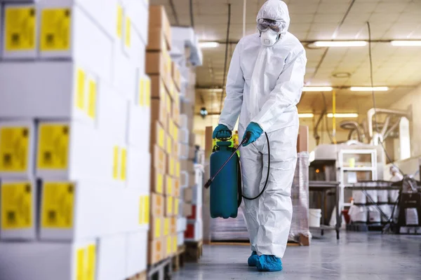 身穿防护服 戴着口罩的男子在仓库里消毒 里面装满了来自Corona病毒 Covid 19的食品 — 图库照片