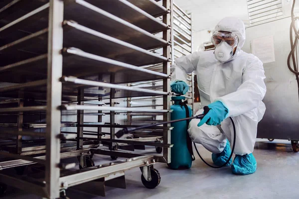 身穿防护服 戴着口罩的男子在仓库里消毒 里面装满了来自Corona病毒 Covid 19的食品 — 图库照片