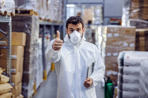 Young man standing in warehouse full of food and showing thumbs up. All warehouse is disinfected from corona virus/ covid-19.