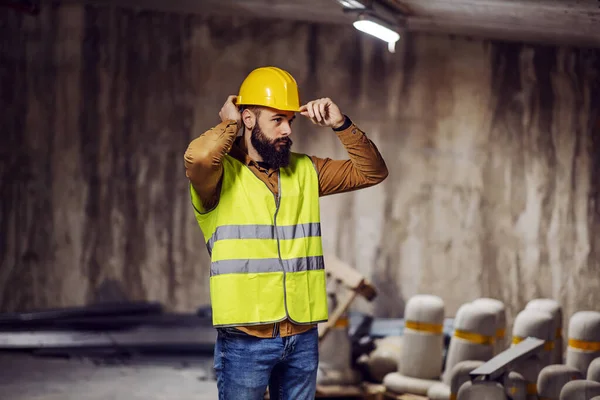 Yelekli Genç Sakallı Işçi Inşaat Aşamasında Binanın Içinde Dikilirken Kaskını — Stok fotoğraf