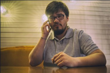 Genç sakallı adam gözlük ve gri gömlek telefon ve ciddi söz oturma. Sağ elinde smartphone ile memnun adam