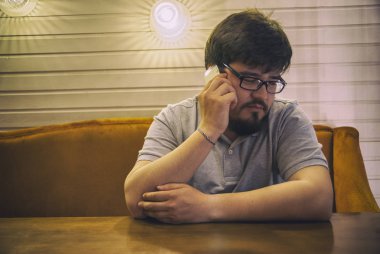 Genç sakallı adam gözlük ve gri gömlek telefon ve memnun söz oturma. Sağ elinde smartphone ile memnun adam