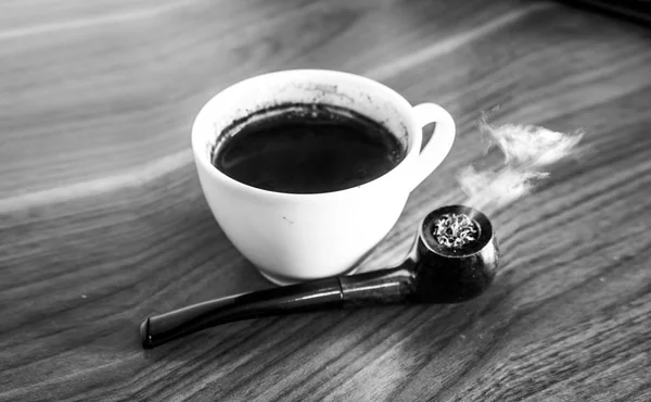 Taza de café negro en una mesa con pipa de fumar iluminada —  Fotos de Stock