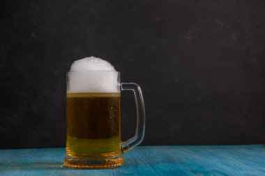 Koyu arkaplanda, ahşap masada bir kupa bira.