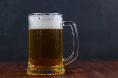 Koyu arkaplanda, ahşap masada bir kupa bira.