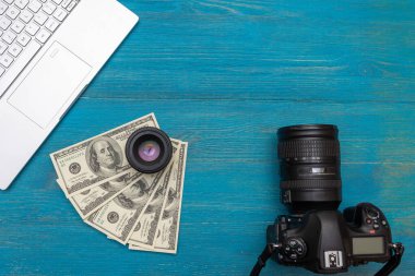 İnternetten para kazan DSR kamera, dolar, laptop, mavi ahşap arka plan, üst görünüm 