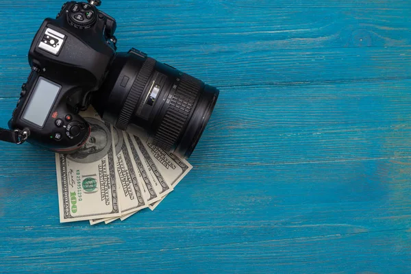 Earn money in internet DSLR camera, dollars, laptop, on blue wooden background, top view