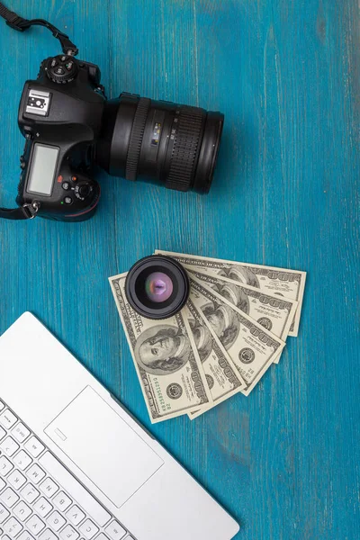 Earn money in internet DSLR camera, dollars, laptop, on blue wooden background, top view