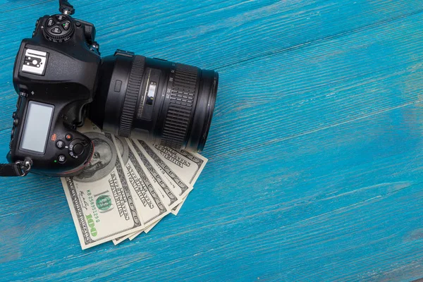 Earn money in internet DSLR camera, dollars, laptop, on blue wooden background, top view