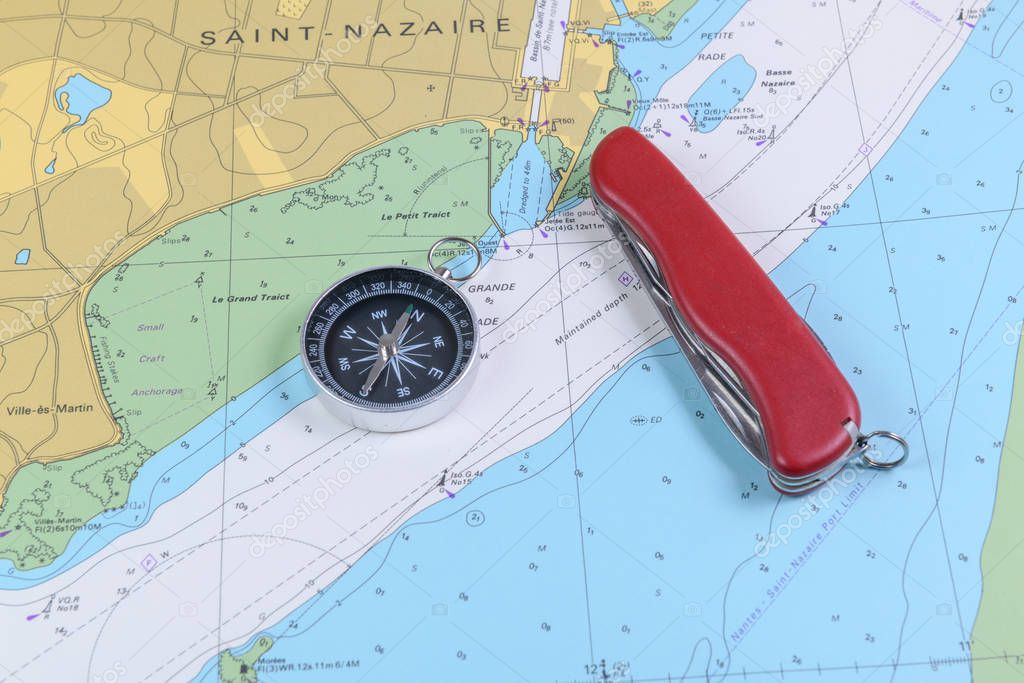 Magnetic compass and folding knife on a nautical navigational map